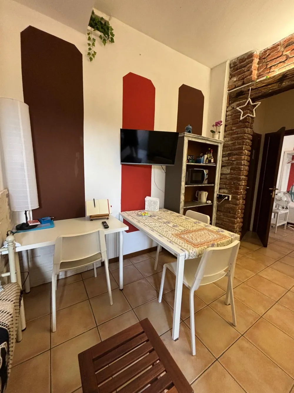 La zona giorno con tavolo, scrivania, televisore a muro e arco in mattoni a vista