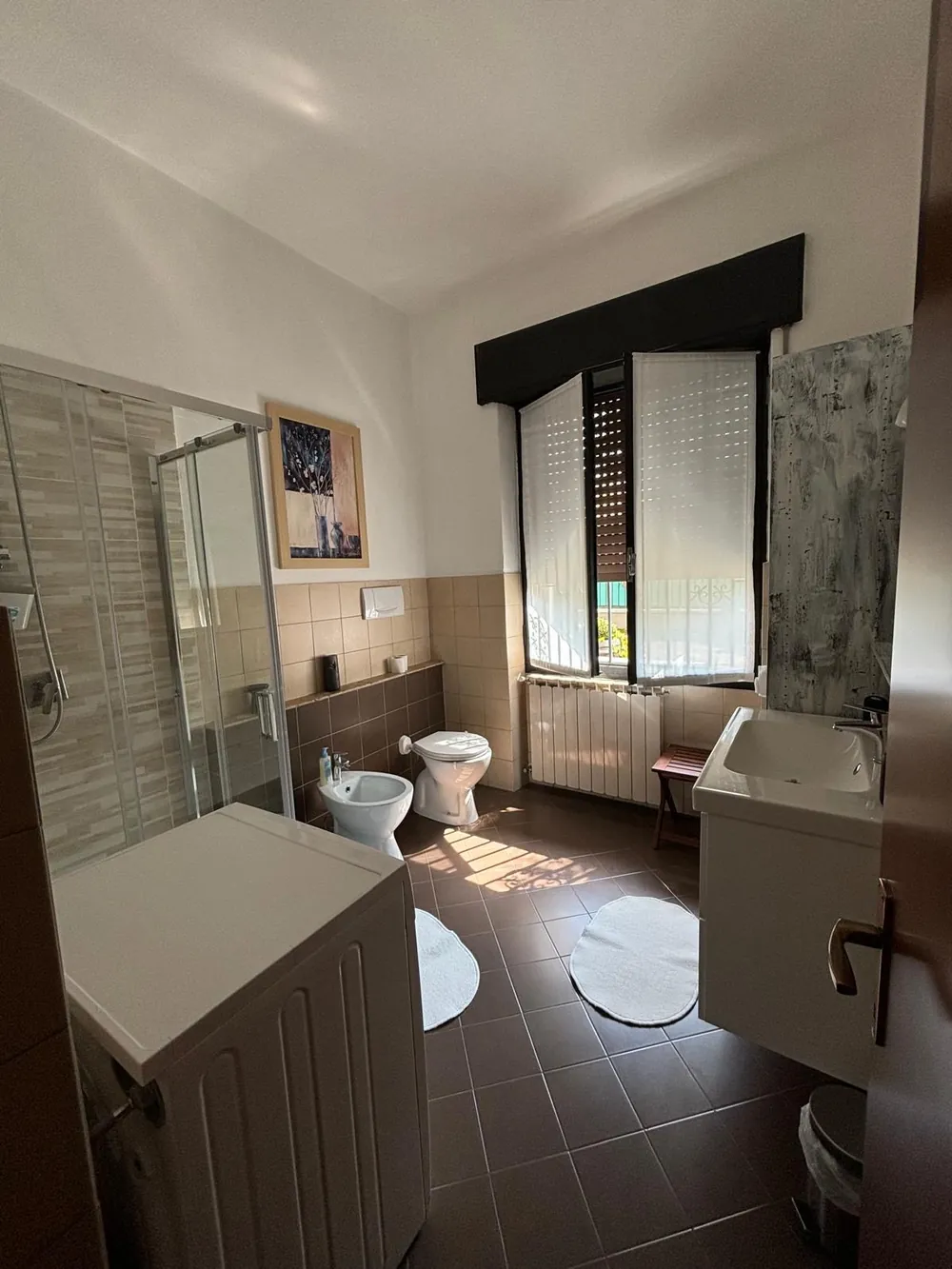 Il bagno con doccia, rivestimento beige e marrone, lavabo e lavatrice